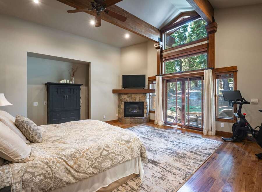 Experience ultimate comfort in this luxurious bedroom, featuring a cozy fireplace and a large window with stunning forest views.