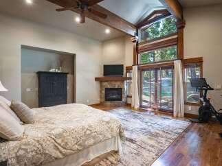Experience ultimate comfort in this luxurious bedroom, featuring a cozy fireplace and a large window with stunning forest views.
