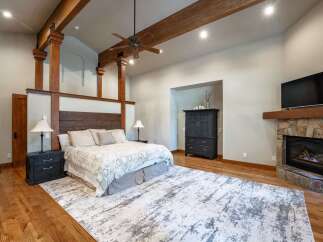 Experience rustic luxury in this master bedroom featuring exposed wooden beams and a stone fireplace.