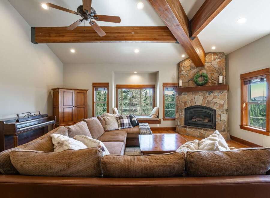 Experience rustic charm in this spacious living room, featuring a grand stone fireplace and exposed wooden beams that add warmth and character.