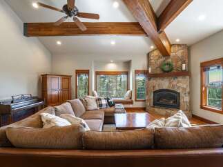 Experience rustic charm in this spacious living room, featuring a grand stone fireplace and exposed wooden beams that add warmth and character.
