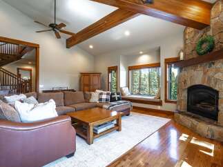Experience rustic elegance in this spacious living room, featuring a grand stone fireplace and exposed wooden beams that create a warm, inviting atmosphere.