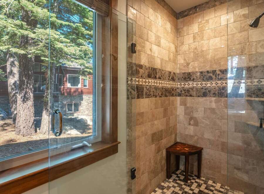 Experience luxury in this stunning bathroom featuring a spacious walk-in shower with elegant marble tile and a built-in wooden bench.