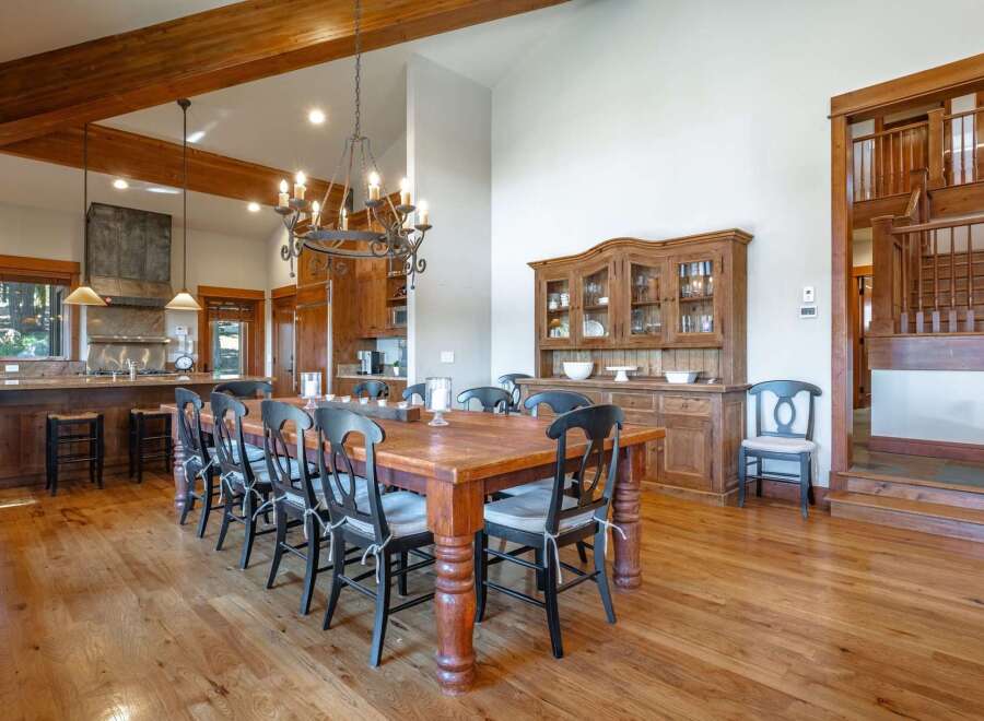 Experience rustic elegance in this spacious dining area, featuring a grand wooden dining table with seating for ten, illuminated by a striking chandelier.