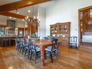 Experience rustic elegance in this spacious dining area, featuring a grand wooden dining table with seating for ten, illuminated by a striking chandelier.