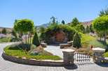 Discover a unique hobbit-inspired home nestled into a hillside, featuring a charming round wooden door and lush landscaping.