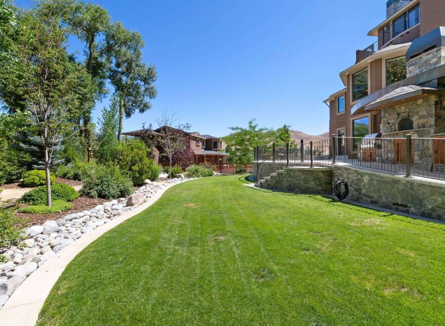 This stunning backyard offers a lush green lawn perfect for recreation and relaxation, bordered by a charming rock garden and mature trees.