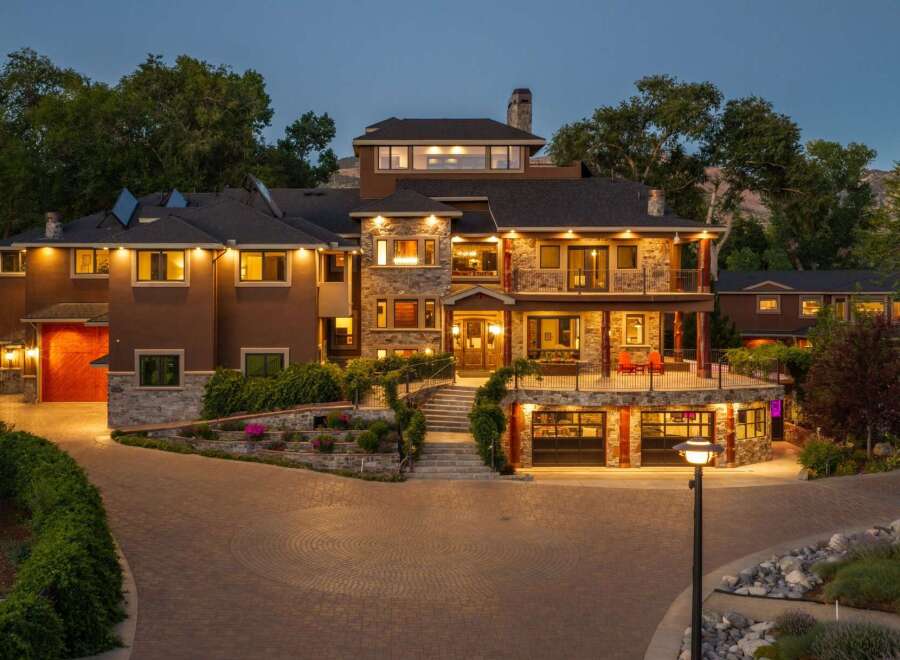 Experience luxury living in this stunning multi-level estate, featuring a grand stone facade and warm, inviting exterior lighting.