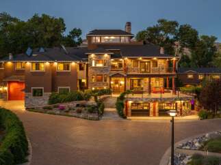Experience luxury living in this stunning multi-level estate, featuring a grand stone facade and warm, inviting exterior lighting.
