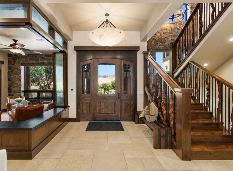 Step into luxury with this grand entryway featuring a stunning double wooden door with glass inlays, offering a picturesque view of the surrounding landscape.