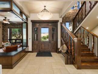 Step into luxury with this grand entryway featuring a stunning double wooden door with glass inlays, offering a picturesque view of the surrounding landscape.