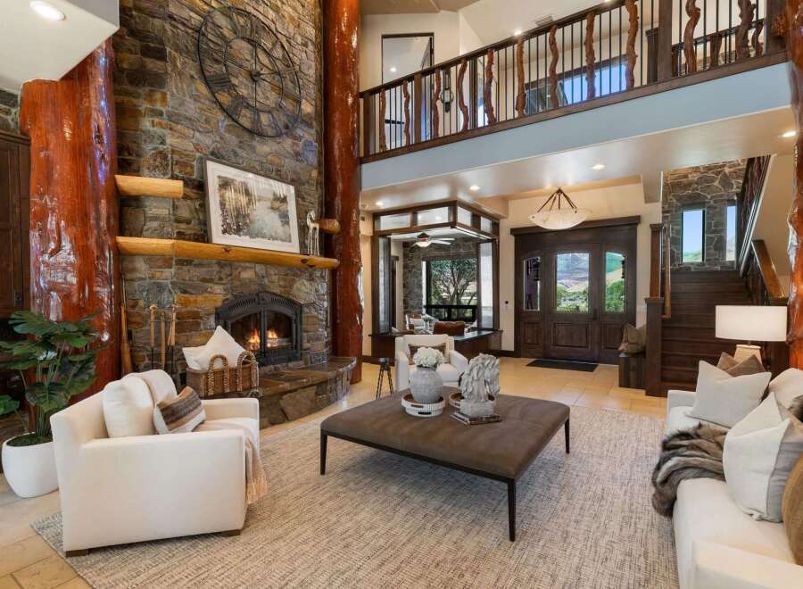 Experience rustic luxury in this grand living room, featuring a towering stone fireplace with a rustic log accent and a large decorative clock.