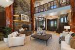 Experience rustic luxury in this grand living room, featuring a towering stone fireplace with a rustic log accent and a large decorative clock.