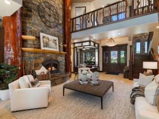 Experience rustic luxury in this grand living room, featuring a towering stone fireplace with a rustic log accent and a large decorative clock.