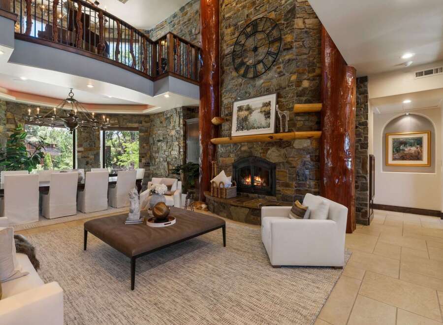 Experience rustic elegance in this grand living space, featuring a towering stone fireplace with a prominent clock and natural wood accents.