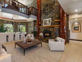Experience rustic elegance in this grand living space, featuring a towering stone fireplace with a prominent clock and natural wood accents.
