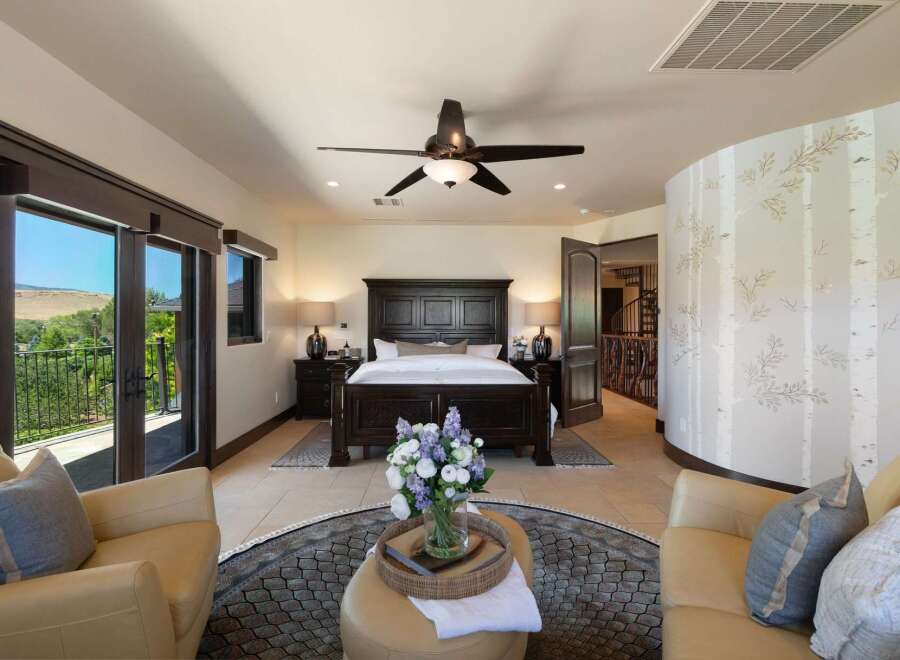 Experience luxury in this master suite featuring a grand dark wood bed and matching nightstands, complemented by a cozy seating area with plush leather chairs.