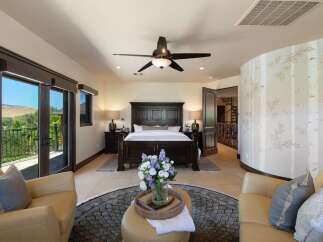 Experience luxury in this master suite featuring a grand dark wood bed and matching nightstands, complemented by a cozy seating area with plush leather chairs.