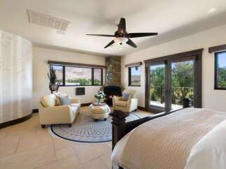 Experience luxury living in this spacious bedroom featuring a cozy stone fireplace and a comfortable seating area.