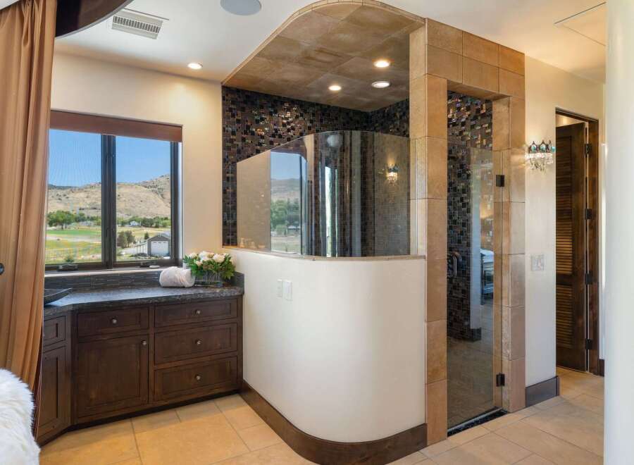 Experience luxury in this master bathroom featuring a stunning curved glass shower with intricate mosaic tile accents.