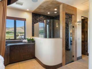 Experience luxury in this master bathroom featuring a stunning curved glass shower with intricate mosaic tile accents.