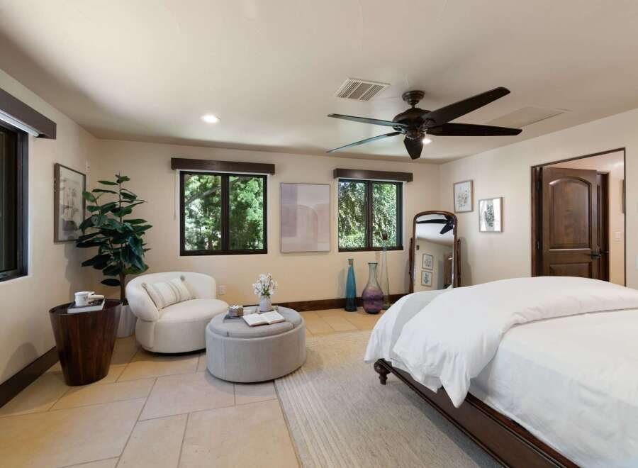 This inviting bedroom offers a serene retreat with ample natural light streaming through large windows, showcasing lush outdoor views.