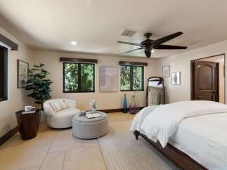 This inviting bedroom offers a serene retreat with ample natural light streaming through large windows, showcasing lush outdoor views.