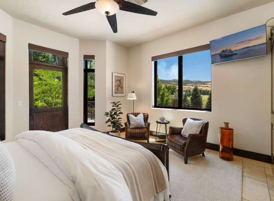 Experience breathtaking mountain views from this luxurious bedroom, featuring a cozy seating area with two leather armchairs and a large picture window.
