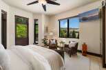 Experience breathtaking mountain views from this luxurious bedroom, featuring a cozy seating area with two leather armchairs and a large picture window.