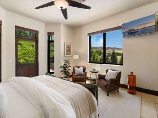 Experience breathtaking mountain views from this luxurious bedroom, featuring a cozy seating area with two leather armchairs and a large picture window.