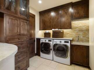 This laundry room boasts custom dark wood cabinetry, providing ample storage and a luxurious feel.