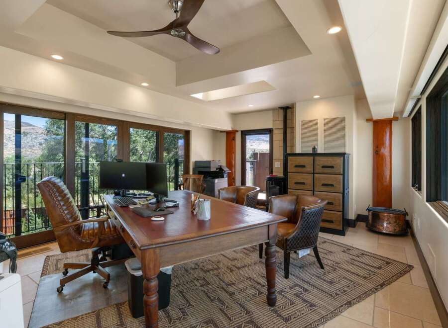 This spacious home office features a large wooden desk with a leather inlay, complemented by a comfortable executive chair and two accent chairs.