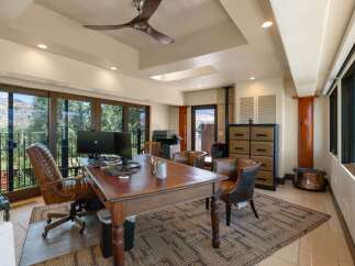 This spacious home office features a large wooden desk with a leather inlay, complemented by a comfortable executive chair and two accent chairs.