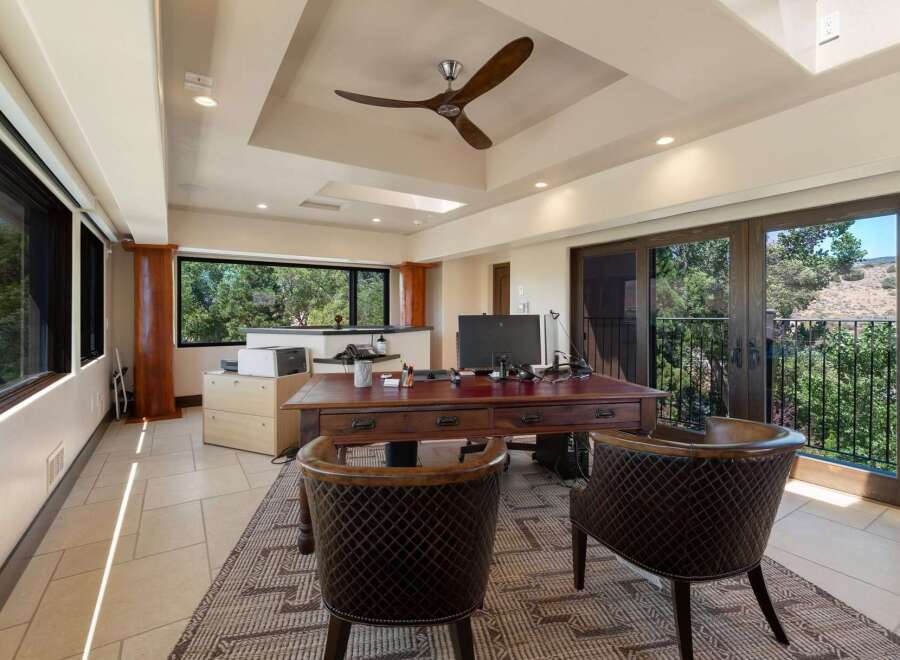 This spacious home office features a large wooden desk with a computer and office supplies, complemented by two plush leather chairs.
