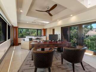 This spacious home office features a large wooden desk with a computer and office supplies, complemented by two plush leather chairs.