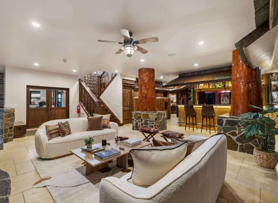 Step into a rustic-chic living space featuring a cozy seating area with plush sofas and a unique tree-trunk-inspired bar.