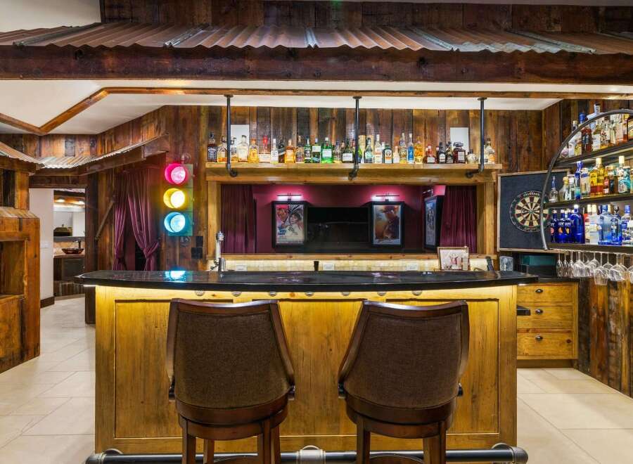 Step into a unique entertainment space featuring a rustic wooden bar with a granite countertop, illuminated by warm under-lighting.