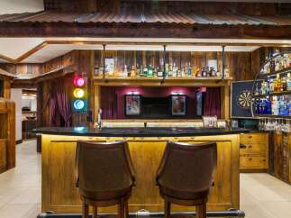 Step into a unique entertainment space featuring a rustic wooden bar with a granite countertop, illuminated by warm under-lighting.