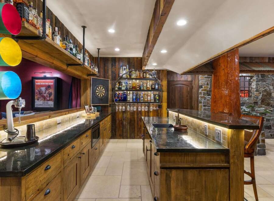 Step into this rustic home bar, featuring a stunning wooden bar top and custom cabinetry.
