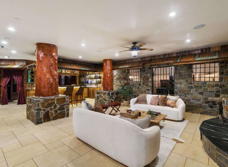 Experience rustic luxury in this unique living space, featuring a full-service bar with ample bottle display and seating, complemented by a striking stone fireplace.