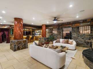 Experience rustic luxury in this unique living space, featuring a full-service bar with ample bottle display and seating, complemented by a striking stone fireplace.