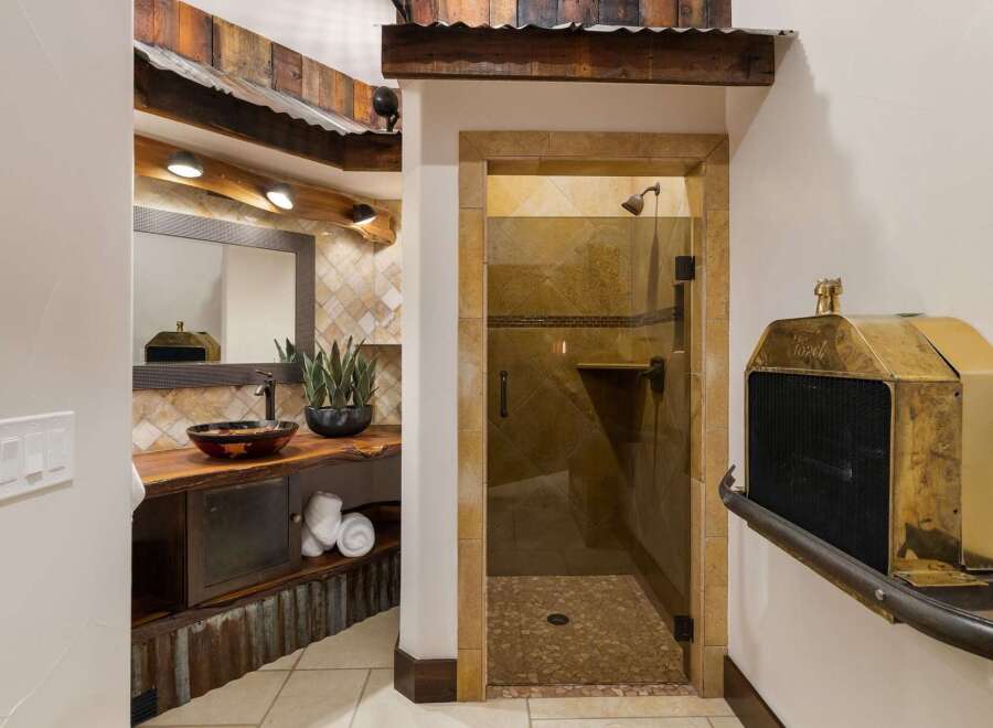 Experience rustic charm in this unique bathroom featuring a live-edge wood vanity with a vessel sink and a spacious walk-in shower with stone tile accents.