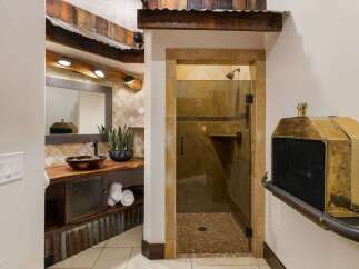 Experience rustic charm in this unique bathroom featuring a live-edge wood vanity with a vessel sink and a spacious walk-in shower with stone tile accents.