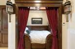 Step into a unique sleeping nook, featuring rich wooden accents and luxurious deep red velvet curtains that create a cozy, private retreat.