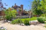 Experience luxurious living in this stunning multi-level home, featuring a spacious backyard with a stone-retaining wall and lush green lawn.