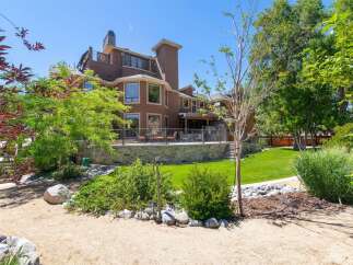 Experience luxurious living in this stunning multi-level home, featuring a spacious backyard with a stone-retaining wall and lush green lawn.