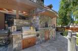 Experience the ultimate outdoor living with this luxurious stone outdoor kitchen, featuring a built-in grill, pizza oven, and ample storage.
