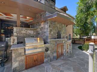 Experience the ultimate outdoor living with this luxurious stone outdoor kitchen, featuring a built-in grill, pizza oven, and ample storage.
