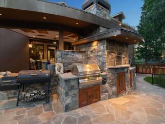 Experience luxury outdoor living with this stunning custom-built outdoor kitchen, featuring a built-in grill, pizza oven, and ample stone counter space.