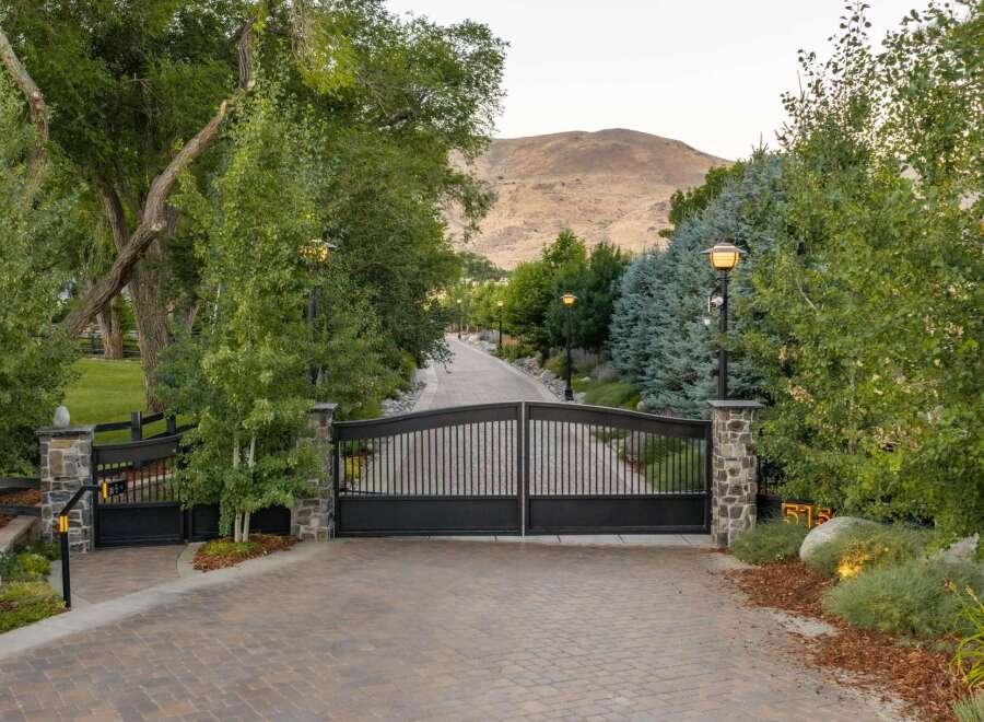 Welcome to this stunning estate, accessed through grand black iron gates and a paved driveway lined with mature trees and elegant lampposts.